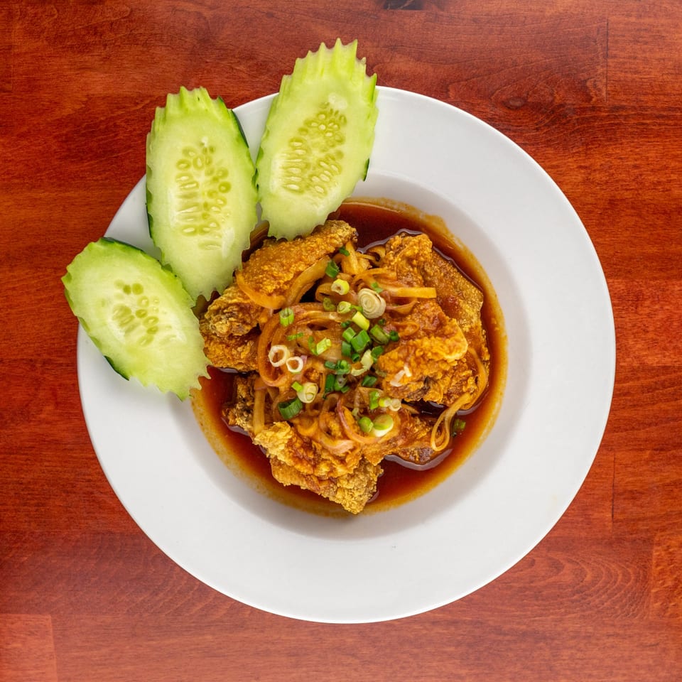 Crispy fried chicken in a rich brown sauce, topped with onions and scallions, served with cucumber slices.