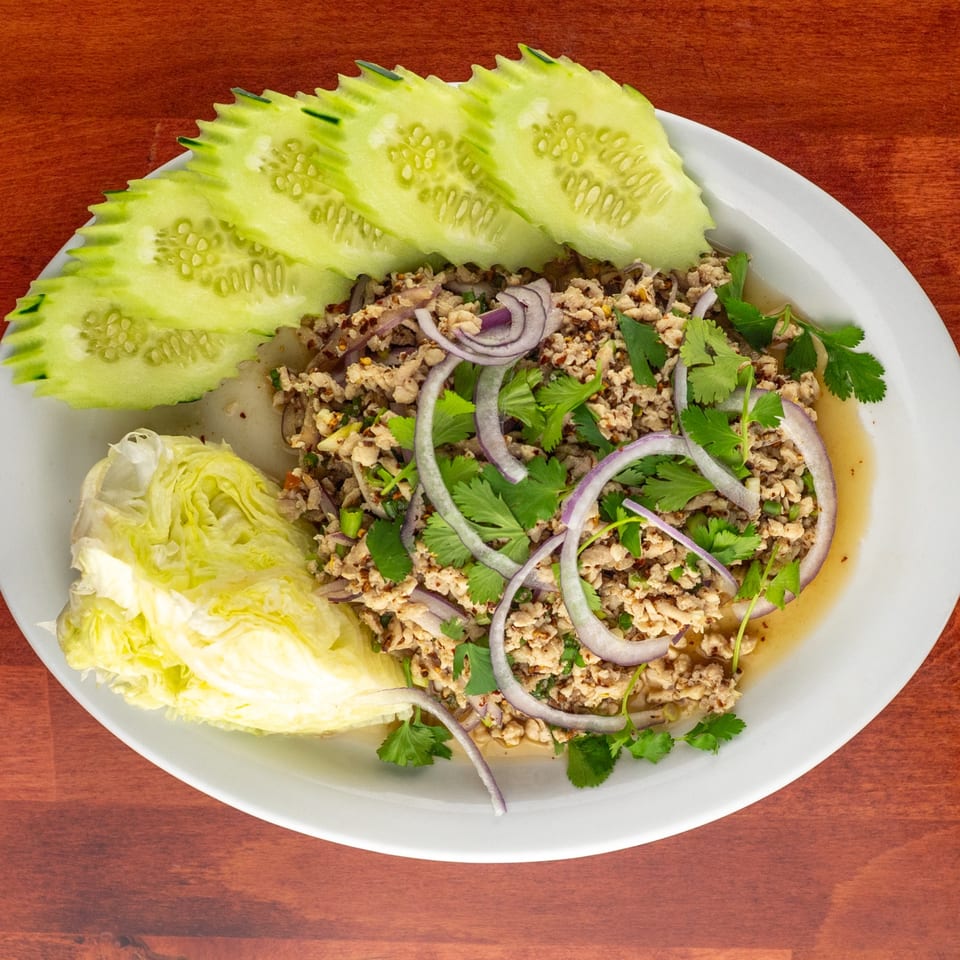 Larb Gai, a Thai minced chicken salad with red onions, cilantro, and chili, served with cucumber and lettuce.